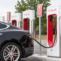 Nakup rabljenega električnega avtomobila: Na kaj morate biti najbolj pozorni? Električni avtomobil Tesla, priključen na Supercharger polnilnico, med polnjenjem na parkirišču ob več zaporednih polnilnih postajah.